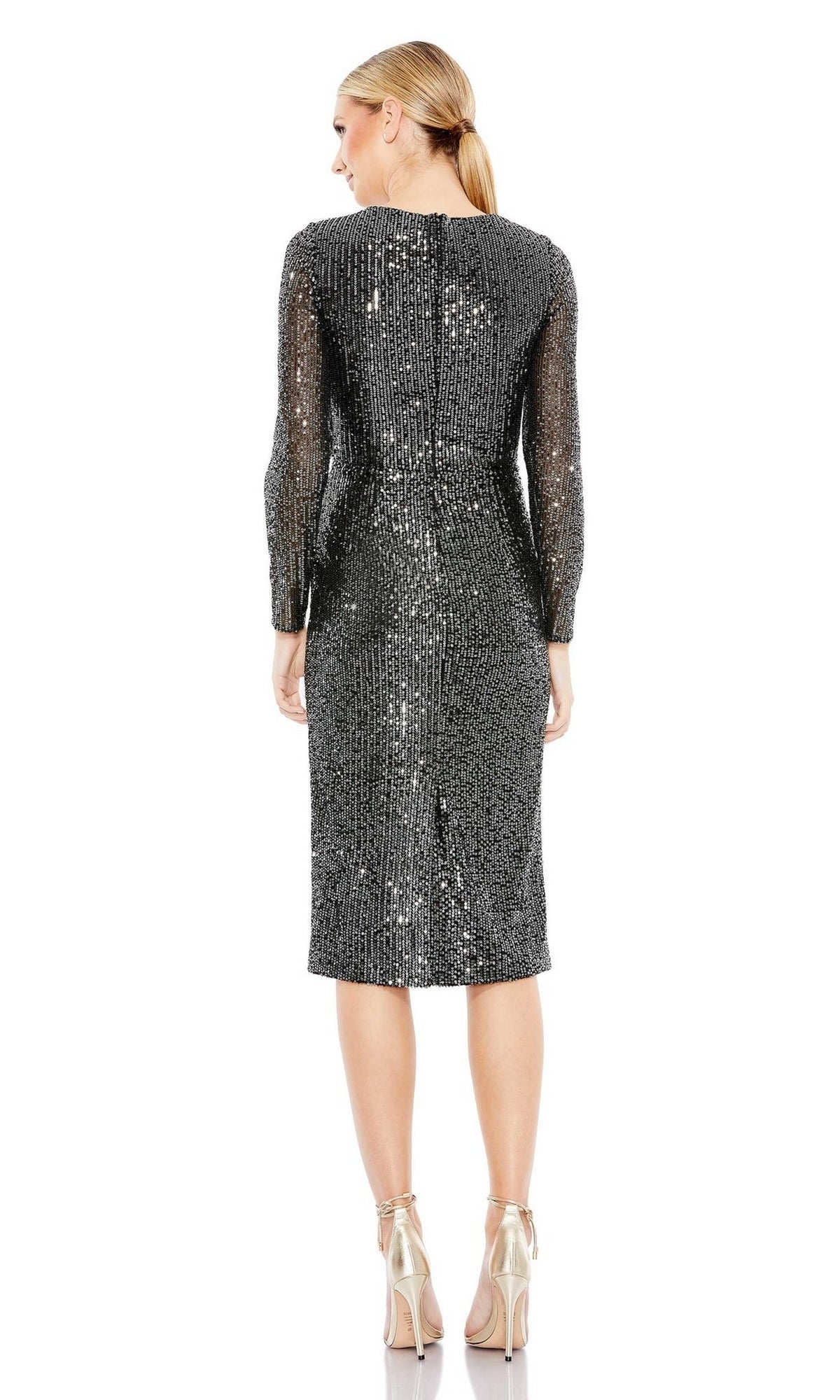 A woman faces away wearing the Short Wedding Guest Dress 26940 by Mac Duggal, a knee-length sequin party dress with long sleeves, paired with metallic high-heeled sandals against a white background.